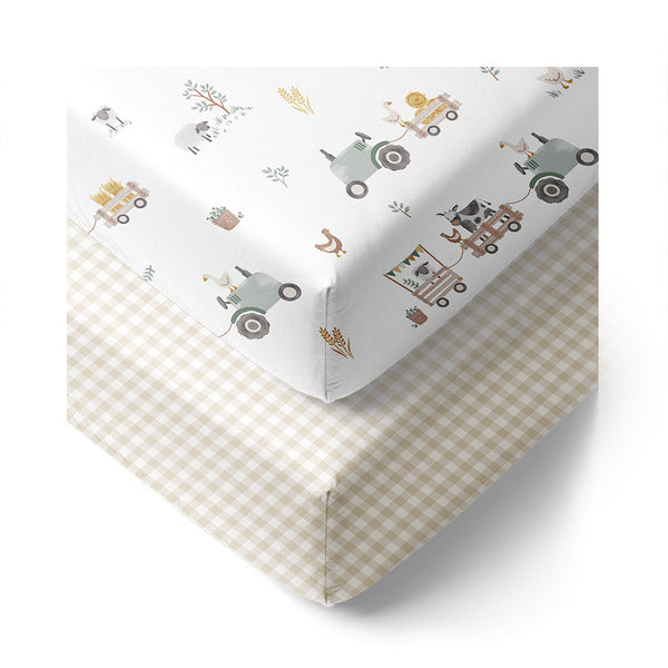 Two fitted cot sheets, one with a tractor ride pattern and the other in a checkered design, laid on a white background.